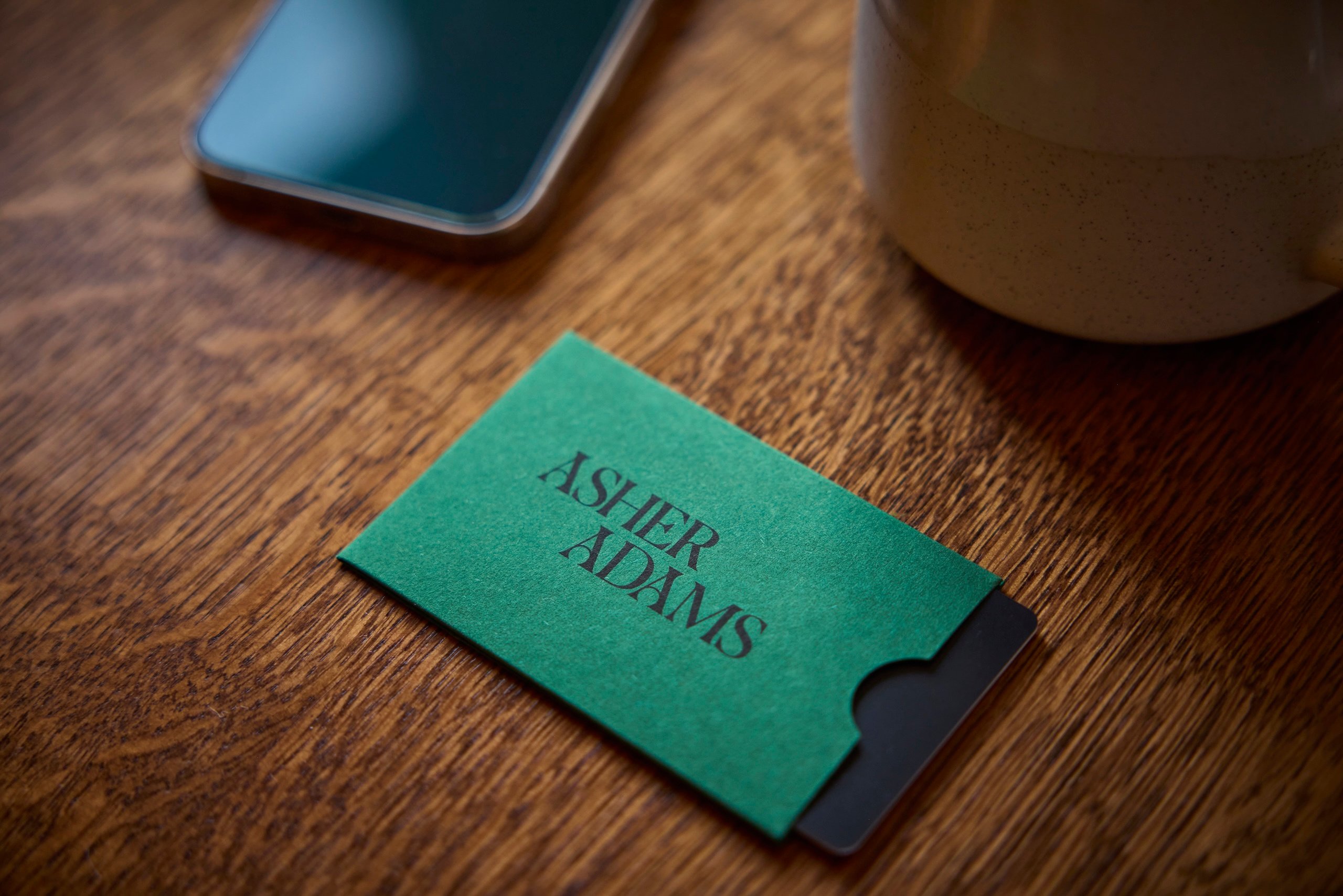 A green hotel key card holder branded with Asher Adams on a wooden table.