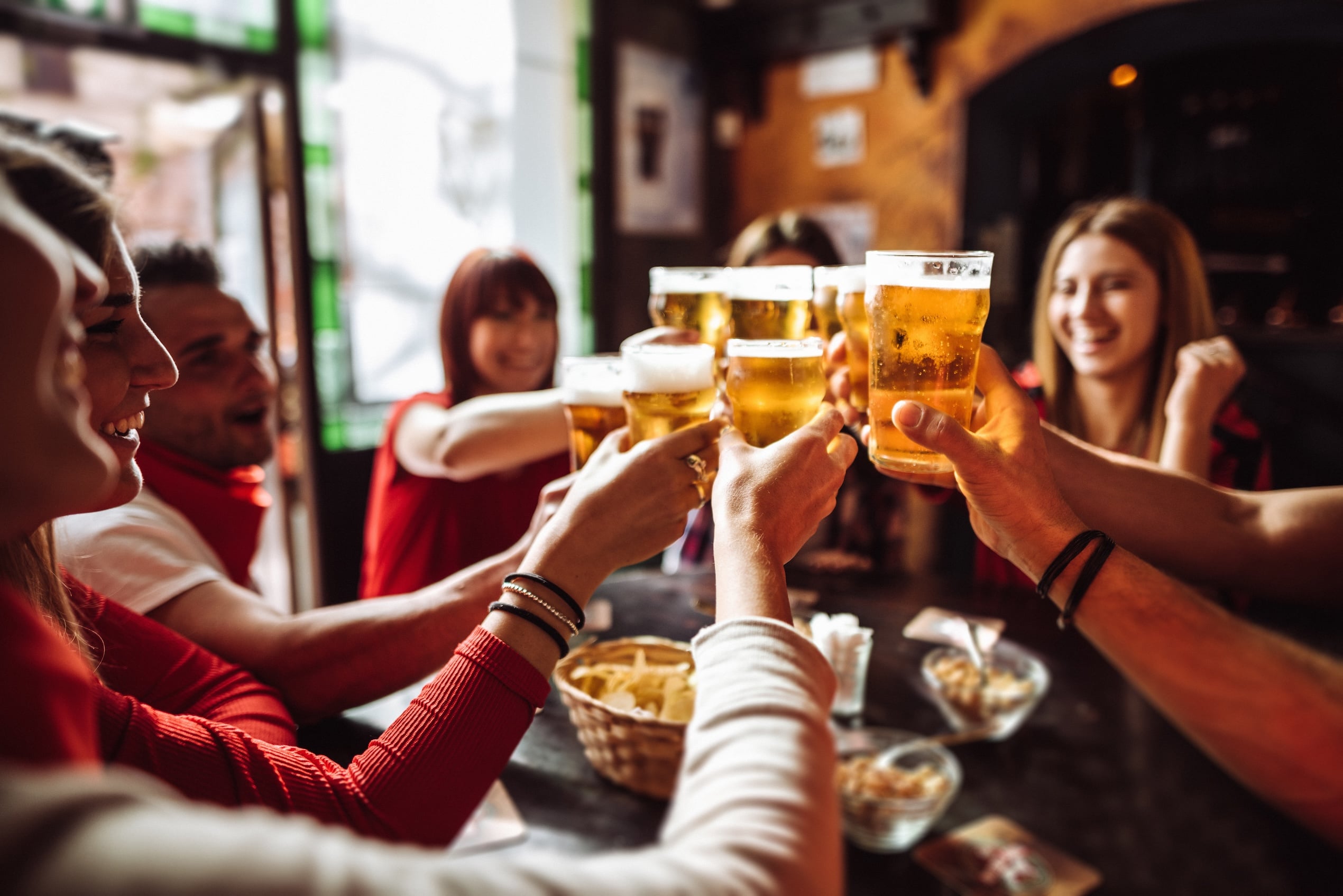 A group of friends toasting pints of beer over pub snacks