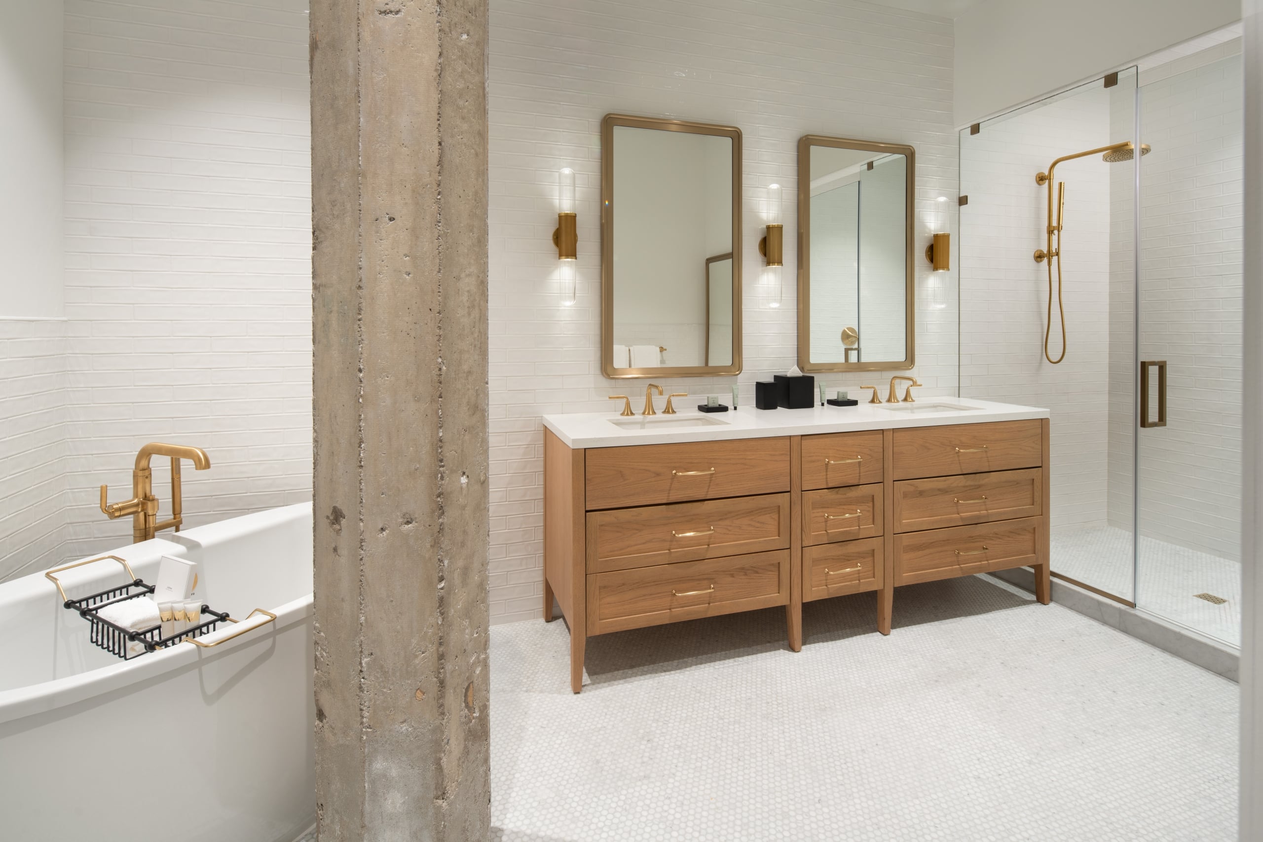 A hotel bathroom with a wooden vanity with two sinks and two mirrors, with a soaker tub on the left, and a glass shower.
